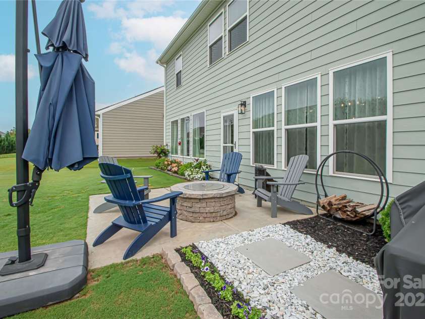 1061 Ansley Park Drive, Fort Mill, SC 29707.  MLS# CAR4281028, YatesRealty ID 32626. The manicured backyard features a cement patio and fire pit—perfect for relaxing or entertaining. Beautiful landscaping includes flowering bushes like azaleas, accented by elegant stonework for added charm.