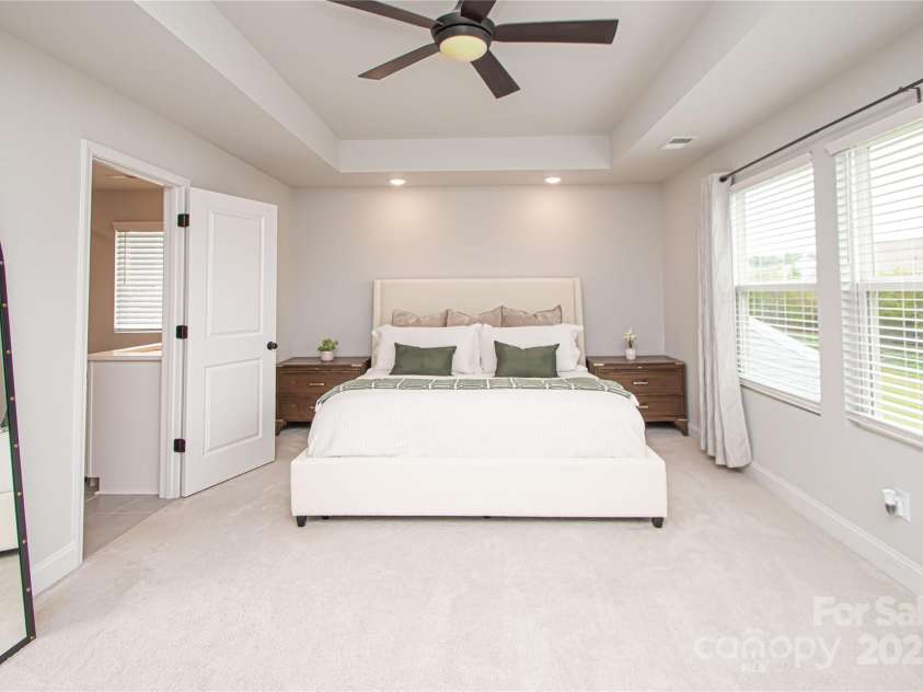 1061 Ansley Park Drive, Fort Mill, SC 29707.  MLS# CAR4281028, YatesRealty ID 32626. The spacious primary bedroom is located on the second floor and features a tray ceiling, ceiling fan with light kit, and large windows that fill the room with natural light.