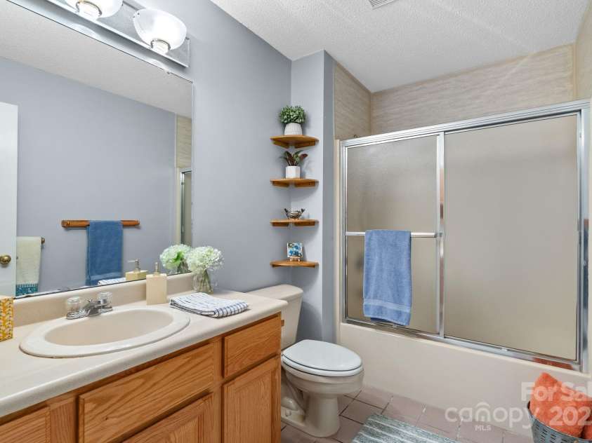 27 Eden Glen Road, Black Mountain, NC 28711.  MLS# CAR4292054, YatesRealty ID 3277. Fresh and functional full bath featuring a wide vanity with plenty of counter space, built-in shelving for storage, and a tub/shower combo with sliding glass doors.