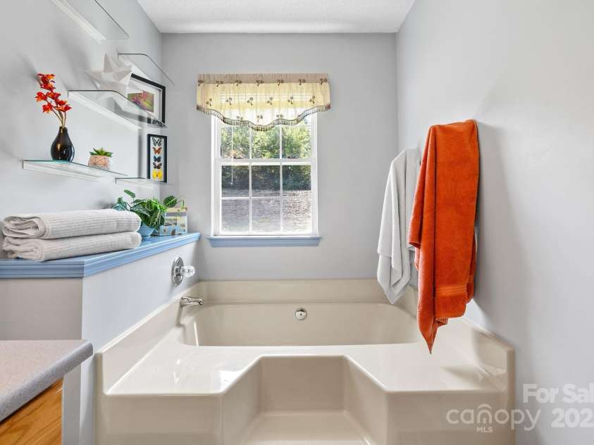 27 Eden Glen Road, Black Mountain, NC 28711.  MLS# CAR4292054, YatesRealty ID 3277. Unwind at the end of the day in this deep soaking tub, perfectly positioned beneath a bright window that fills the space with natural light. Thoughtful shelving adds charm and functionality, making this bathroom as s