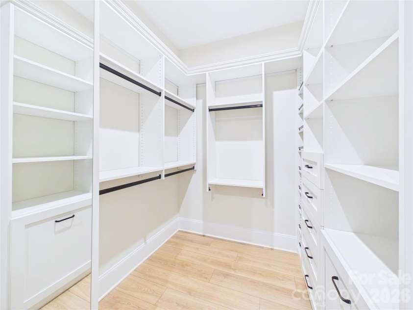 8027 Longwaters Court, York, SC 29745.  MLS# CAR4368751, YatesRealty ID 33228. This expansive walk-in closet features a custom-built organization system with floor-to-ceiling white shelving, drawers, and dedicated hanging space. The room is enhanced by a large built-in mirror that adds a sense of de