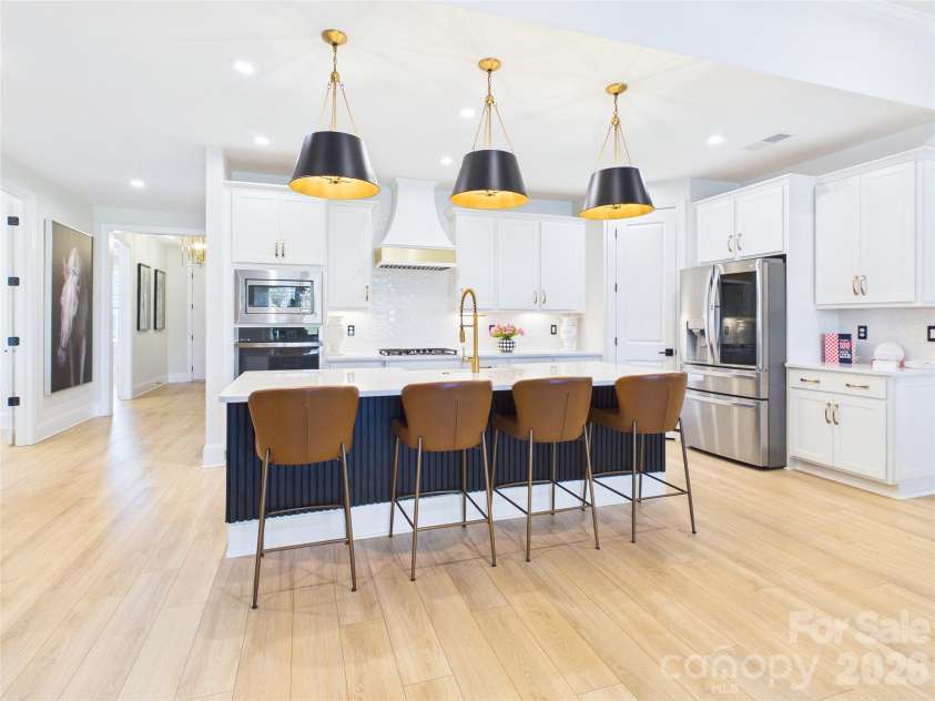 8027 Longwaters Court, York, SC 29745.  MLS# CAR4368751, YatesRealty ID 33228. This modern open-concept kitchen features a large central island with a fluted base and elegant gold-accented pendant lighting. The space is anchored by crisp white cabinetry and high-end, upgraded stainless steel applian