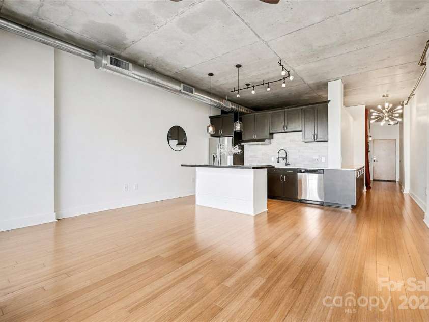 505 6th Street, Charlotte, NC 28202.  MLS# CAR4331119, YatesRealty ID 3329. Interior – Kitchen and Living AreaSpacious open-concept design with exposed concrete ceilings, bamboo flooring, and a sleek kitchen with updated cabinetry, stainless appliances, and pendant lighting.