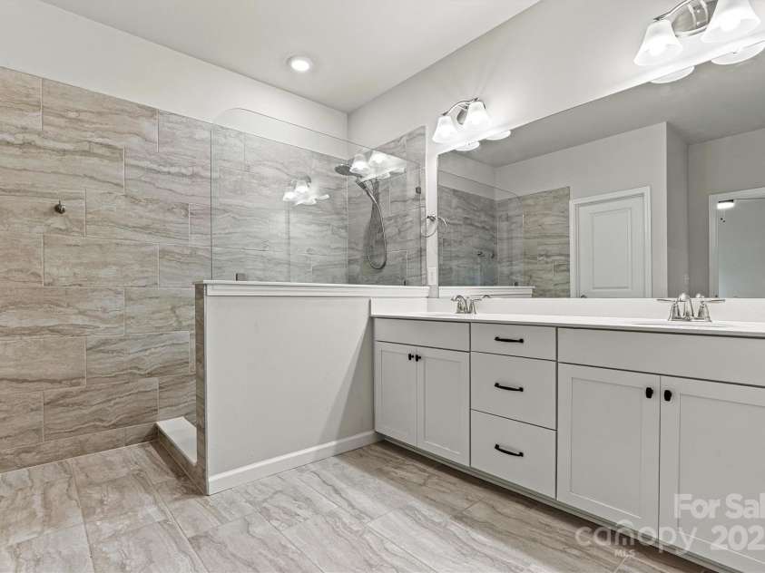 8233 Merryvale Lane, Charlotte, NC 28214.  MLS# CAR4293433, YatesRealty ID 34155. Step into the luxurious primary ensuite featuring dual sinks, a spacious walk-in tiled shower, elegant tile flooring, and direct access to the generous walk-in closet—designed for both comfort and style.