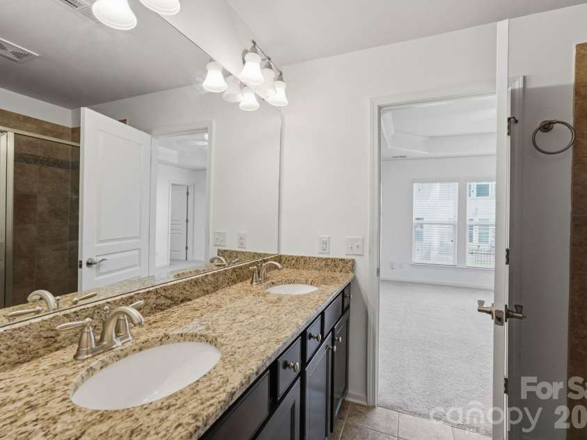 2433 Diplomat Lane, Charlotte, NC 28210.  MLS# CAR4399381, YatesRealty ID 34720. Spacious primary bath with granite double vanity, dark cabinetry, large mirror, and tiled glass-enclosed shower.