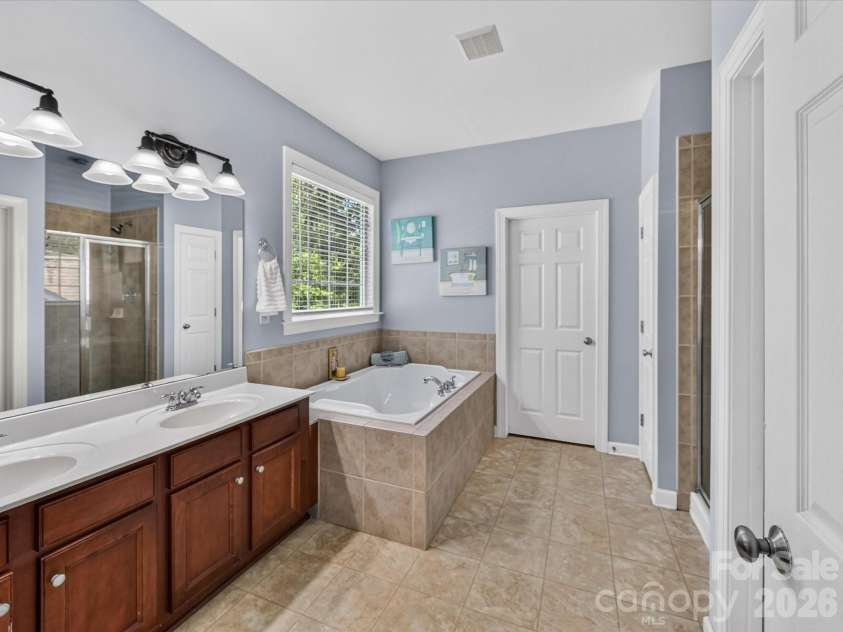 18625 The Commons Boulevard, Cornelius, NC 28031.  MLS# CAR4397710, YatesRealty ID 36310. The spacious primary bath features dual vanities, a relaxing soaking tub, a separate glass-enclosed shower, and a linen closet, creating a comfortable spa-like retreat.