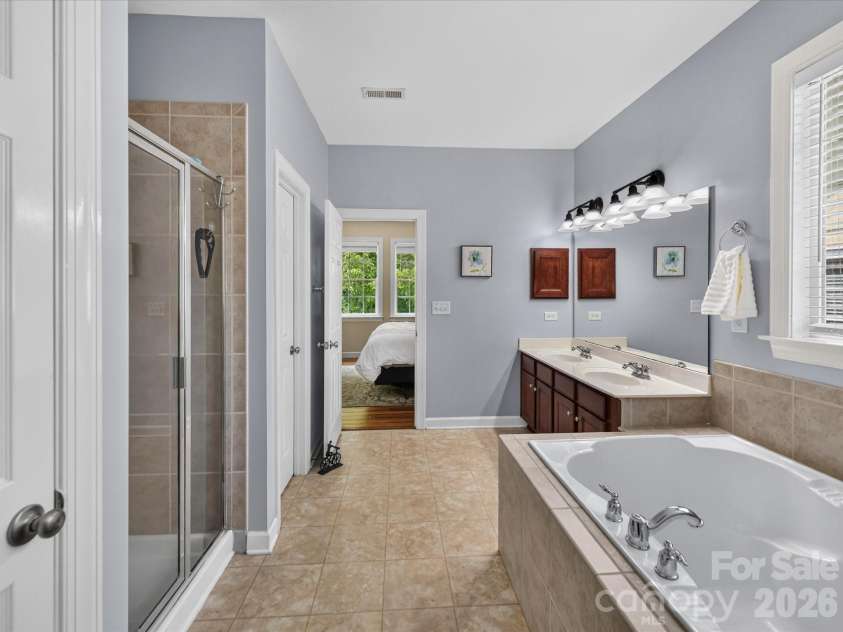 18625 The Commons Boulevard, Cornelius, NC 28031.  MLS# CAR4397710, YatesRealty ID 36310. The spacious primary bath features dual vanities, a relaxing soaking tub, a separate glass-enclosed shower, and a linen closet, creating a comfortable spa-like retreat.