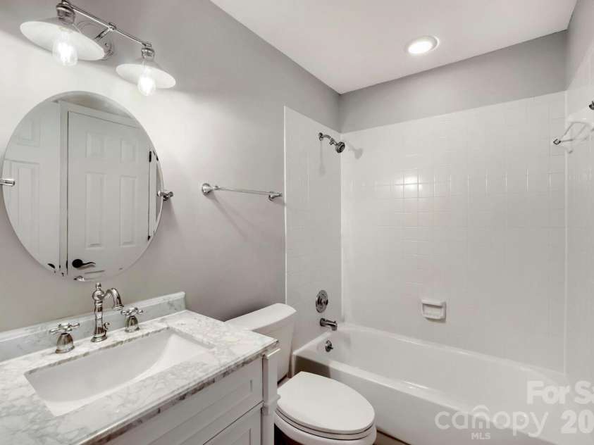 2520 Stradbrook Drive, Charlotte, NC 28210.  MLS# CAR4396722, YatesRealty ID 380. Second Bath: A round mirror and marble-topped vanity bring elegance to this full secondary bath, complete with a classic tub/shower combo. Crisp white tile keeps the space feeling clean and bright.