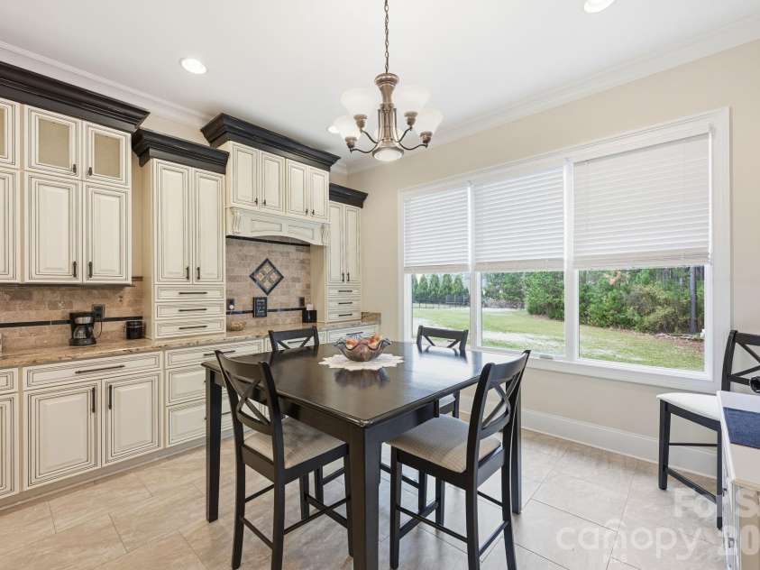 108 Washam Road, Mooresville, NC 28117.  MLS# CAR4334255, YatesRealty ID 4048. Bright dining area adjacent to the kitchen, featuring custom cabinetry, tile flooring, and a stylish chandelier overhead. Large windows provide abundant natural light and peaceful views of the backyard, creating an inviti