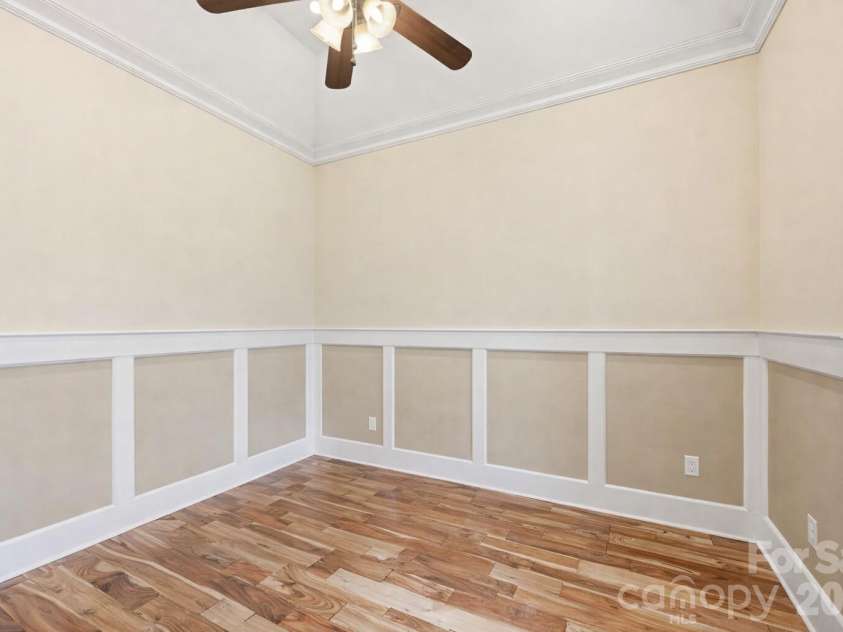 108 Washam Road, Mooresville, NC 28117.  MLS# CAR4334255, YatesRealty ID 4048. Bright home office featuring hardwood floors, wainscoting, and crown molding with a ceiling fan overhead. The space offers ample natural light and open wall space, making it ideal for a workspace, hobby room, or study.