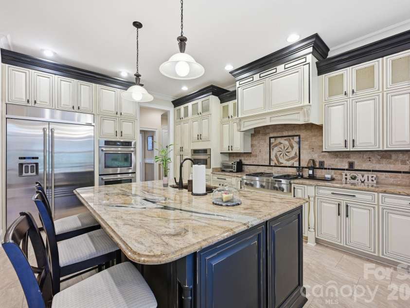 108 Washam Road, Mooresville, NC 28117.  MLS# CAR4334255, YatesRealty ID 4048. Elegant kitchen showcasing custom cabinetry, granite countertops, and a large center island with seating. The space features stainless steel appliances, pendant lighting, and a decorative tile backsplash, creating a brigh