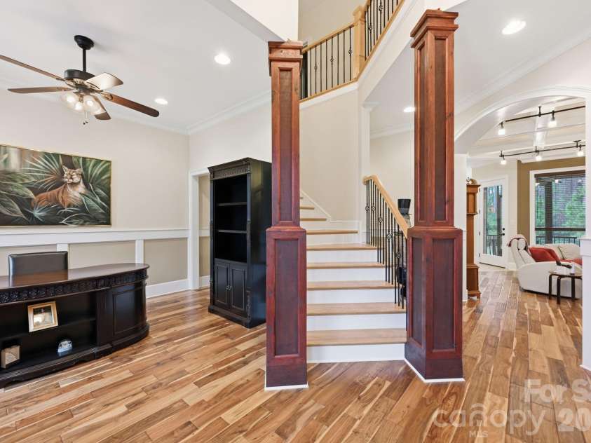 108 Washam Road, Mooresville, NC 28117.  MLS# CAR4334255, YatesRealty ID 4048. Open interior space featuring hardwood floors, a central staircase with wood railing, and views into adjacent living areas. The layout feels bright and spacious with clean architectural lines and an inviting flow between 