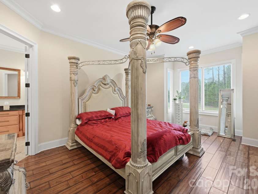 108 Washam Road, Mooresville, NC 28117.  MLS# CAR4334255, YatesRealty ID 4048. Spacious primary bedroom featuring hardwood floors, large windows with natural light, and an elegant four-poster bed as the focal point. The room offers a bright, airy feel with crown molding and direct access to an adjoi