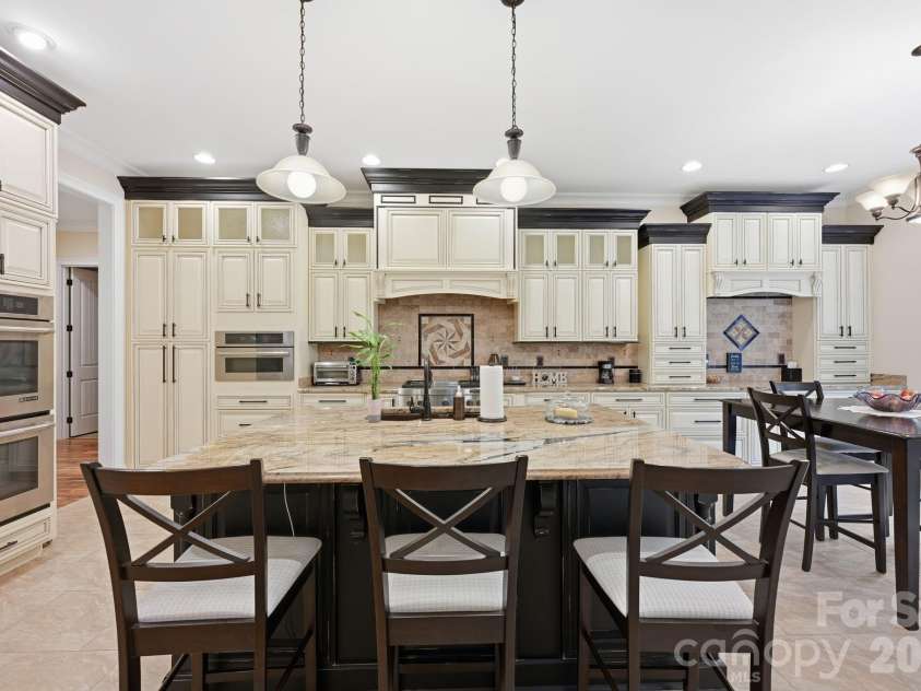 108 Washam Road, Mooresville, NC 28117.  MLS# CAR4334255, YatesRealty ID 4048. Spacious, upscale kitchen featuring custom cabinetry, granite countertops, and a large center island with seating. Pendant lighting and stainless steel appliances enhance the bright, open layout that flows seamlessly into