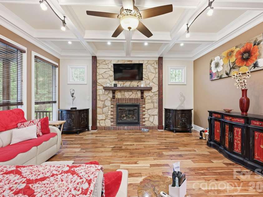 108 Washam Road, Mooresville, NC 28117.  MLS# CAR4334255, YatesRealty ID 4048. Warm and inviting living area featuring hardwood floors, a coffered ceiling with ceiling fan, and a stone fireplace with mounted television as the focal point. The room offers large windows for natural light and built-in 