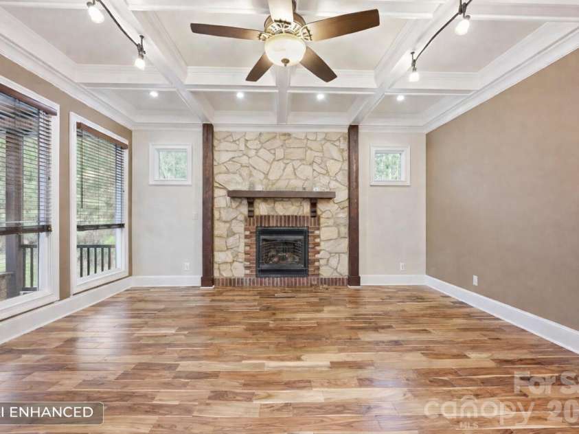 108 Washam Road, Mooresville, NC 28117.  MLS# CAR4334255, YatesRealty ID 4048. Warm and inviting living area featuring hardwood floors, a coffered ceiling with ceiling fan, and a stone fireplace with mounted television as the focal point. The room offers large windows for natural light and built-in 