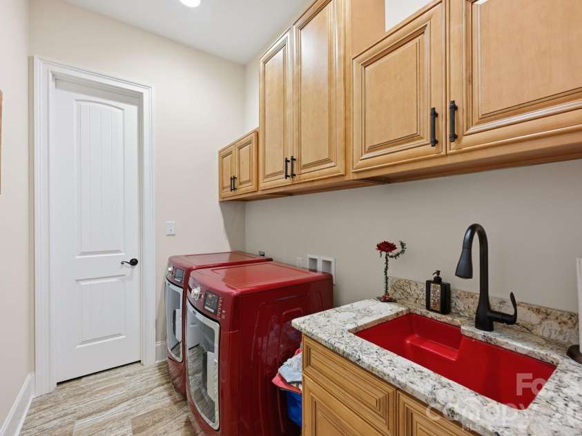108 Washam Road, Mooresville, NC 28117.  MLS# CAR4334255, YatesRealty ID 4048. Well-appointed laundry room featuring custom cabinetry, granite countertops, and a deep utility sink. The space offers tile flooring, overhead storage, and room for full-size washer and dryer, providing a functional and o
