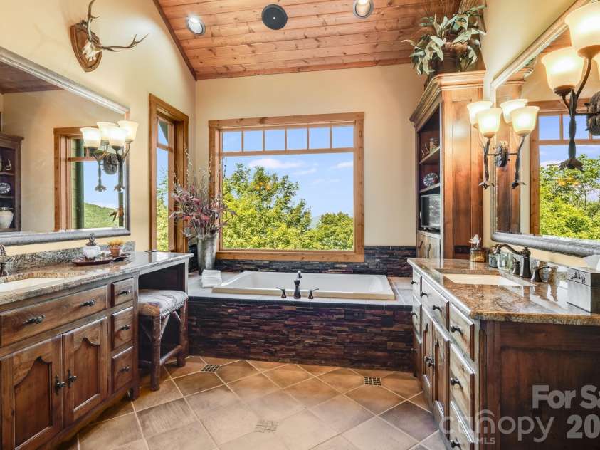 817 Running Cedar Lane, Mars Hill, NC 28754.  MLS# CAR4407984, YatesRealty ID 42073. The beautifully appointed primary bath features dual vanities, custom cabinetry and a jetted soaking tub positioned beneath an expansive mountain view window.