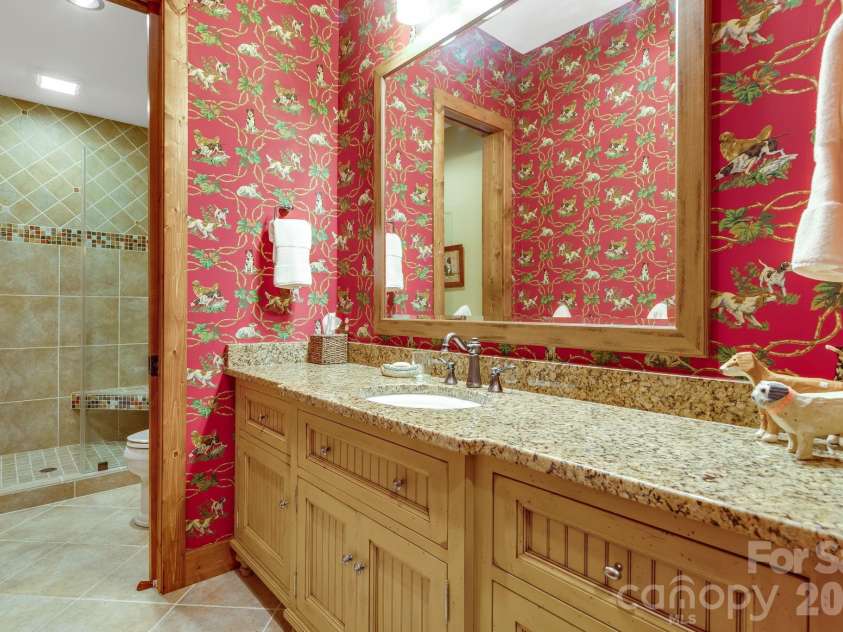 817 Running Cedar Lane, Mars Hill, NC 28754.  MLS# CAR4407984, YatesRealty ID 42073. The bunk room’s full bath brings a playful touch with distinctive dog-patterned wallpaper, a granite-topped vanity and a glass enclosed tiled shower.