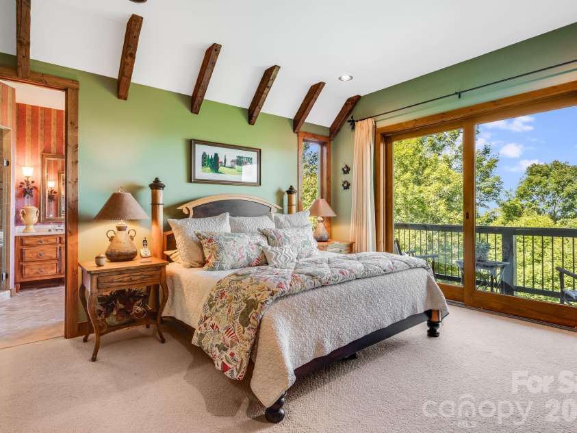 817 Running Cedar Lane, Mars Hill, NC 28754.  MLS# CAR4407984, YatesRealty ID 42073. The lower-level primary suite features a vaulted ceiling with exposed timber rafters, a private ensuite bath and direct walkout access to the covered deck overlooking the mountains.