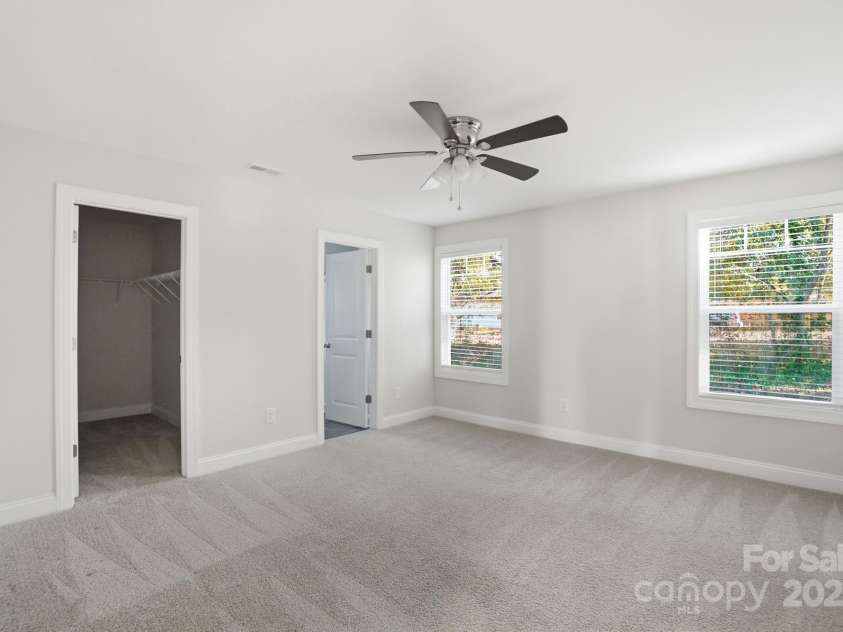 351 Center Street, Kannapolis, NC 28083.  MLS# CAR4304032, YatesRealty ID 4248. The tranquil primary bedroom offers a peaceful retreat with soft grey carpeting, abundant natural light, a modern ceiling fan, and easy access to a walk-in closet