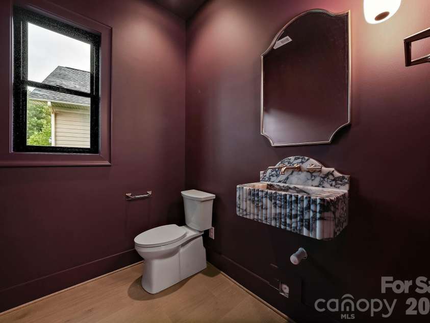 21617 Rio Oro Drive, Cornelius, NC 28031.  MLS# CAR4411277, YatesRealty ID 43438. Dramatic color-drenched powder room featuring a wall-mounted Calcutta Viola marble sink, designer sconce lighting, and rich hardwood floors - a bold, sophisticated statement.