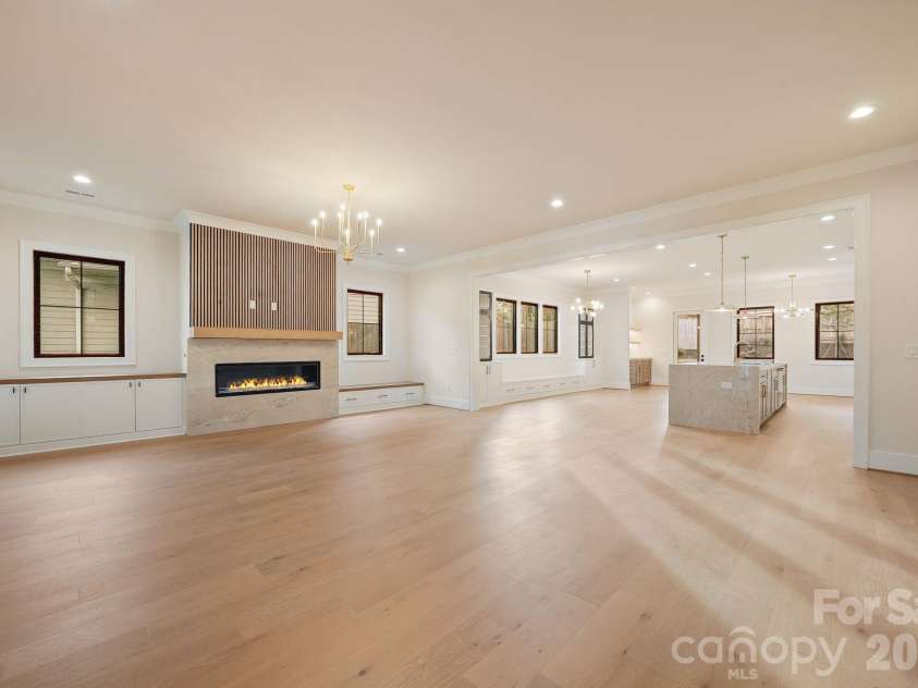 21617 Rio Oro Drive, Cornelius, NC 28031.  MLS# CAR4411277, YatesRealty ID 43438. Open-concept living area featuring a linear fireplace with quartzite surround, white oak fluted paneling, hardwood floors, and abundant built-in storage flowing into the kitchen.