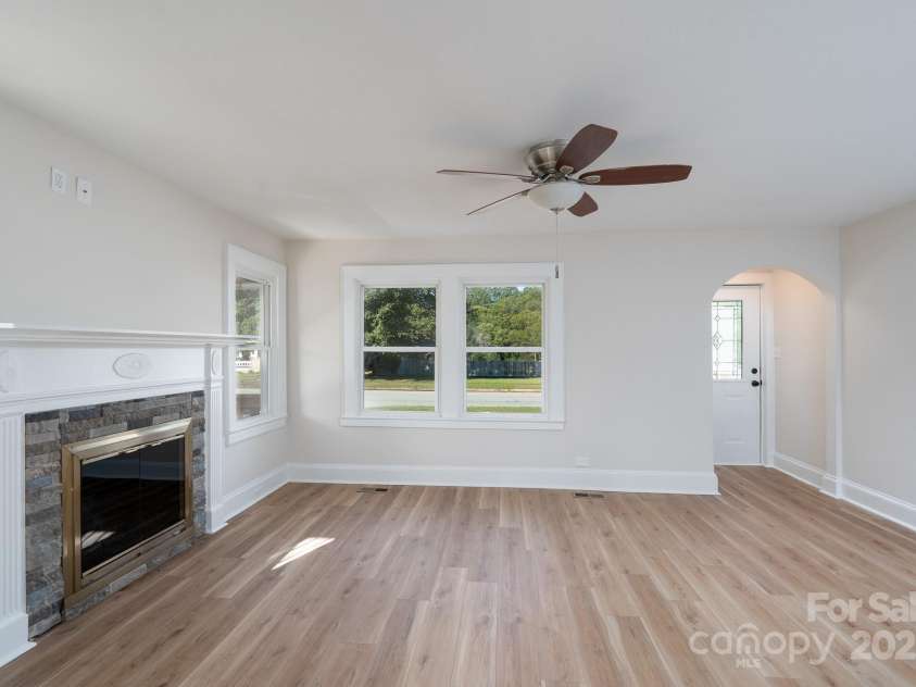 702 3rd Street, Spencer, NC 28159.  MLS# CAR4309115, YatesRealty ID 43594. Looking from the dining room to the living room. Front door entrance to the right corner. Ceiling fan and fireplace with mantle. New LVP flooring. 