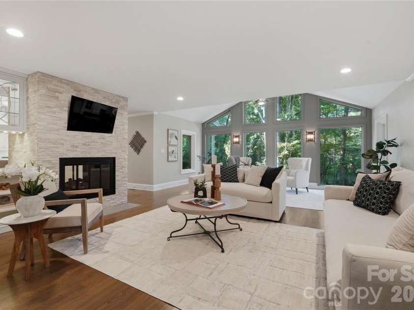 5023 Gorham Drive, Charlotte, NC 28226.  MLS# CAR4402221, YatesRealty ID 44262. An impressive open concept living space where a double sided stone fireplace connects multiple gathering areas, while walls of windows frame the lush greenery beyond.