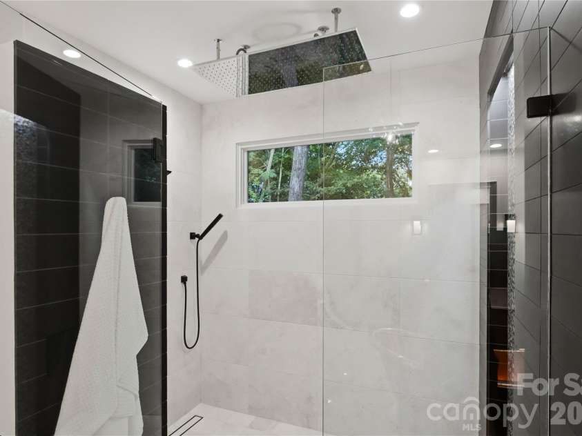 5023 Gorham Drive, Charlotte, NC 28226.  MLS# CAR4402221, YatesRealty ID 44262. Experience a five-star spa every day. The luxurious primary bath features an oversized walk-in shower with dual rainfall showerheads, designer tile, premium fixtures, and expansive windows overlooking the peaceful wooded