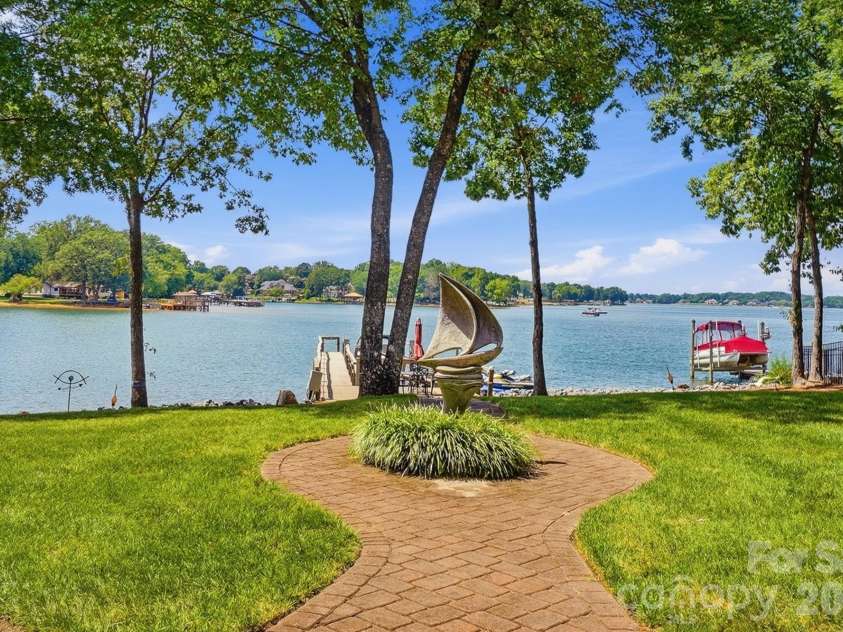 20124 Bascom Ridge Drive, Cornelius, NC 28031.  MLS# CAR4408389, YatesRealty ID 44623. A beautifully manicured lawn and winding brick pathway create a graceful approach to the water, framed by mature shade trees and expansive Lake Norman views. The private dock sits just beyond, reinforcing the home