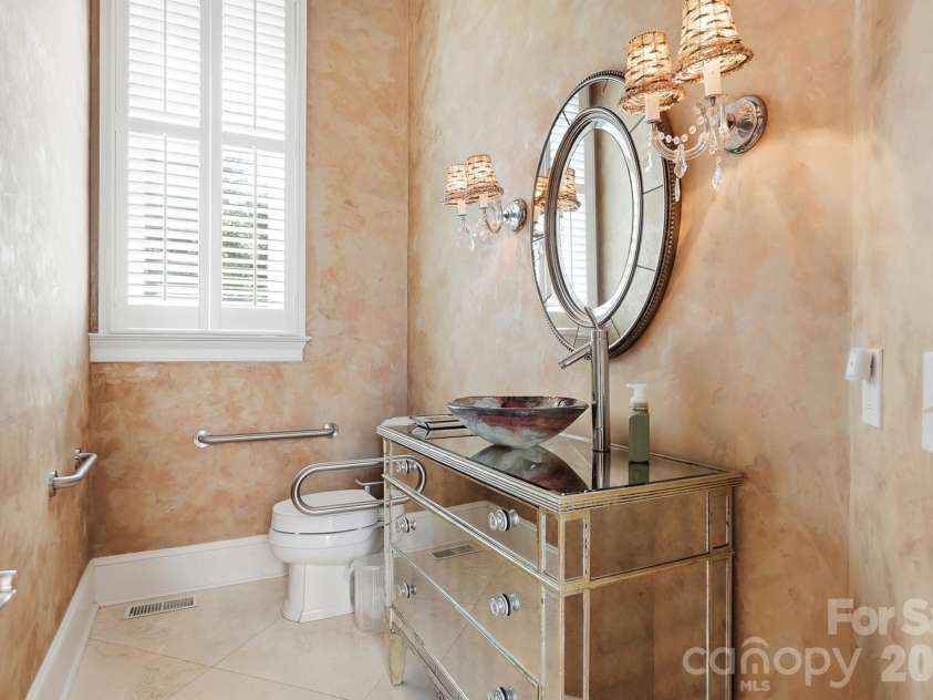 20124 Bascom Ridge Drive, Cornelius, NC 28031.  MLS# CAR4408389, YatesRealty ID 44623. A stylish powder room adds a distinctive touch with a vessel sink, mirrored vanity, decorative sconces, and softly textured walls, while the window brings in natural light.