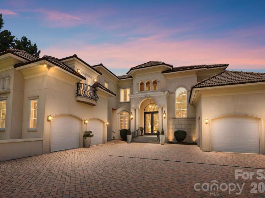 20124 Bascom Ridge Drive, Cornelius, NC 28031.  MLS# CAR4408389, YatesRealty ID 44623. An impressive twilight view showcases the home’s grand Mediterranean-inspired façade, highlighted by warm architectural lighting and a dramatic arched entry. Multiple rooflines, elegant stucco detailing, wrought-i