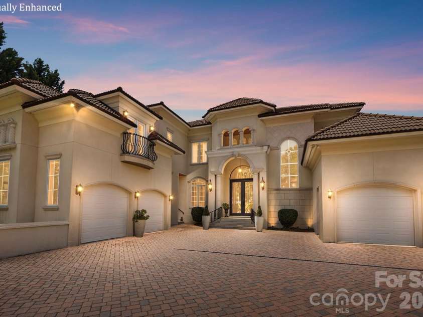 20124 Bascom Ridge Drive, Cornelius, NC 28031.  MLS# CAR4408389, YatesRealty ID 44623. An impressive twilight view showcases the home’s grand Mediterranean-inspired façade, highlighted by warm architectural lighting and a dramatic arched entry. Multiple rooflines, elegant stucco detailing, wrought-i