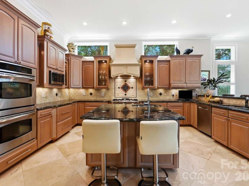 20124 Bascom Ridge Drive, Cornelius, NC 28031.  MLS# CAR4408389, YatesRealty ID 44623. Continuing from the entertaining areas, the spacious kitchen blends warmth and function with rich custom cabinetry, expansive stone countertops, and a large center island with additional seating. Stainless-steel a
