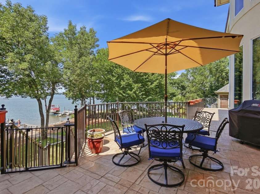 20124 Bascom Ridge Drive, Cornelius, NC 28031.  MLS# CAR4408389, YatesRealty ID 44623. Stepping outside, the expansive terrace creates an inviting setting for outdoor dining and entertaining, with wrought-iron railings, shaded seating, and elevated views across Lake Norman toward the private dock.