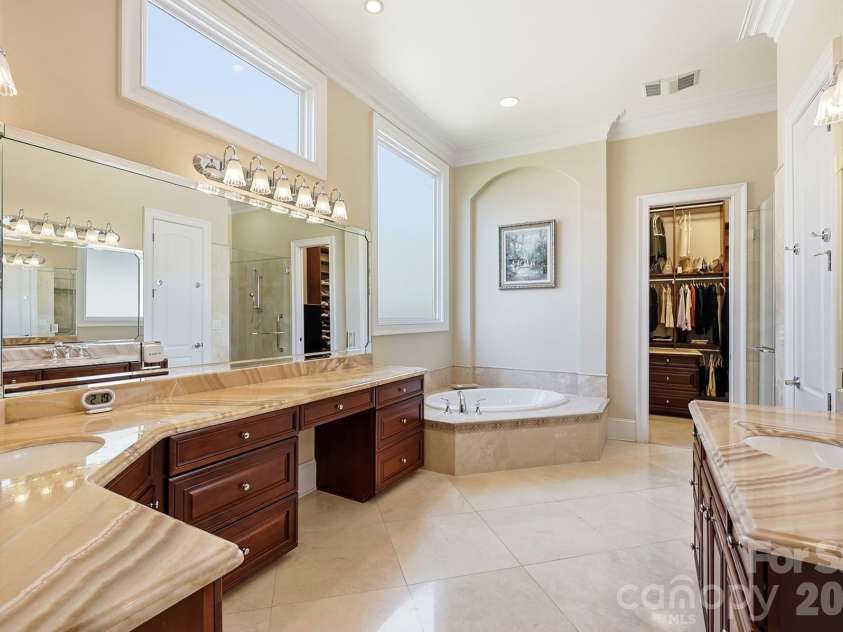 20124 Bascom Ridge Drive, Cornelius, NC 28031.  MLS# CAR4408389, YatesRealty ID 44623. The adjoining primary bath is generously sized and thoughtfully designed with dual vanities, extensive cabinetry, expansive stone countertops, a soaking tub, and a separate glass-enclosed shower. High ceilings and