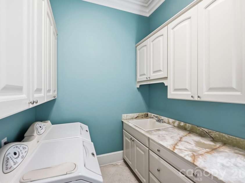 20124 Bascom Ridge Drive, Cornelius, NC 28031.  MLS# CAR4408389, YatesRealty ID 44623. The dedicated laundry room combines practicality with generous storage, featuring extensive cabinetry, a utility sink, and a long stone countertop that provides ample folding and workspace.