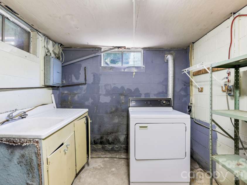 27 McGee Circle, Fairview, NC 28730.  MLS# CAR4415904, YatesRealty ID 45673. Dedicated utility area includes laundry equipment, a utility sink, shelving, and additional storage space.
