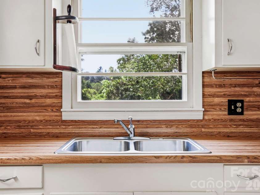 27 McGee Circle, Fairview, NC 28730.  MLS# CAR4415904, YatesRealty ID 45673. Double-basin kitchen sink is positioned beneath a large window overlooking the surrounding greenery.