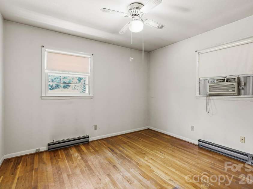 27 McGee Circle, Fairview, NC 28730.  MLS# CAR4415904, YatesRealty ID 45673. Hardwood floors, two windows, a ceiling fan, and baseboard heating provide a practical foundation for this bedroom.