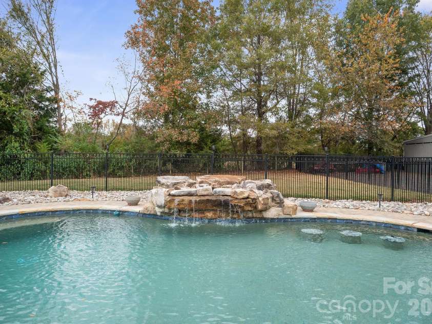 277 Glenwood Drive, Oakboro, NC 28129.  MLS# CAR4312178, YatesRealty ID 45923. Salt water pool has 6 ton natural stone waterfall, 3 barstools and underwater benches, surrounded by pavers and natural stone, secured with black aluminum fencing