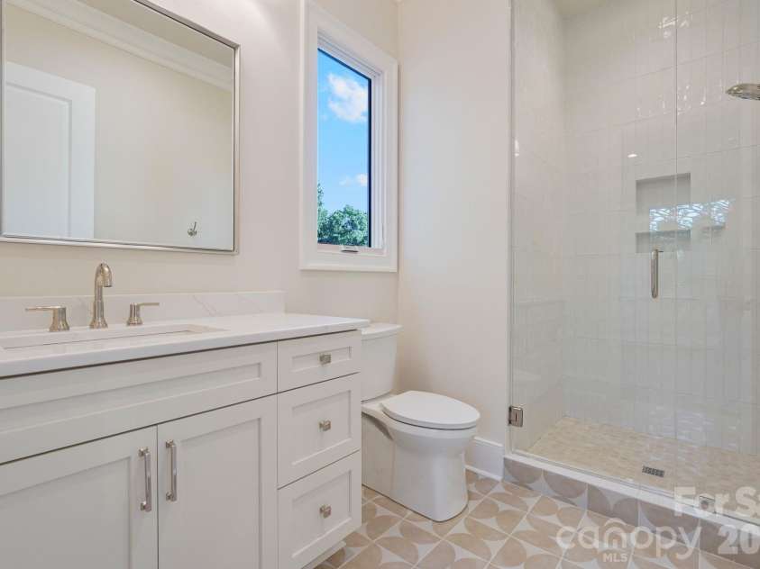 21216 Rio Oro Drive, Cornelius, NC 28031.  MLS# CAR4425303, YatesRealty ID 45943. Bedroom 2 ensuite bath features floor-to-ceiling tile and a thoughtfully placed window that fills the space with natural light, creating a bright, elevated finish.