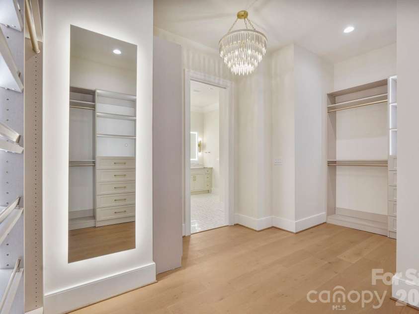21216 Rio Oro Drive, Cornelius, NC 28031.  MLS# CAR4425303, YatesRealty ID 45943. Boutique-inspired primary closet featuring oversized LED mirrors, custom built-ins, and a statement light fixture, creating an elevated space designed for getting ready in style.