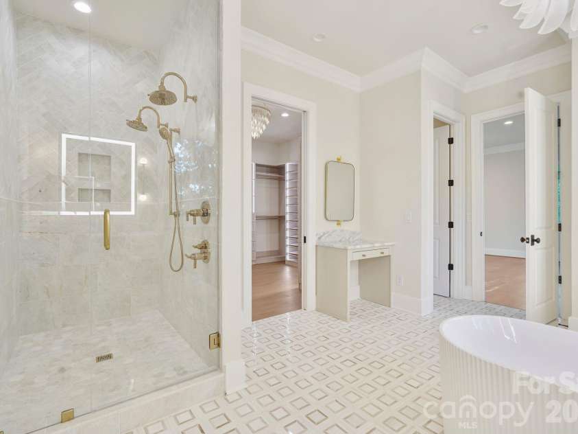 21216 Rio Oro Drive, Cornelius, NC 28031.  MLS# CAR4425303, YatesRealty ID 45943. Luxurious marble shower featuring dual shower heads, floor-to-ceiling tile, and expansive frameless glass, complemented by a dedicated makeup vanity for a truly spa-inspired primary bath.