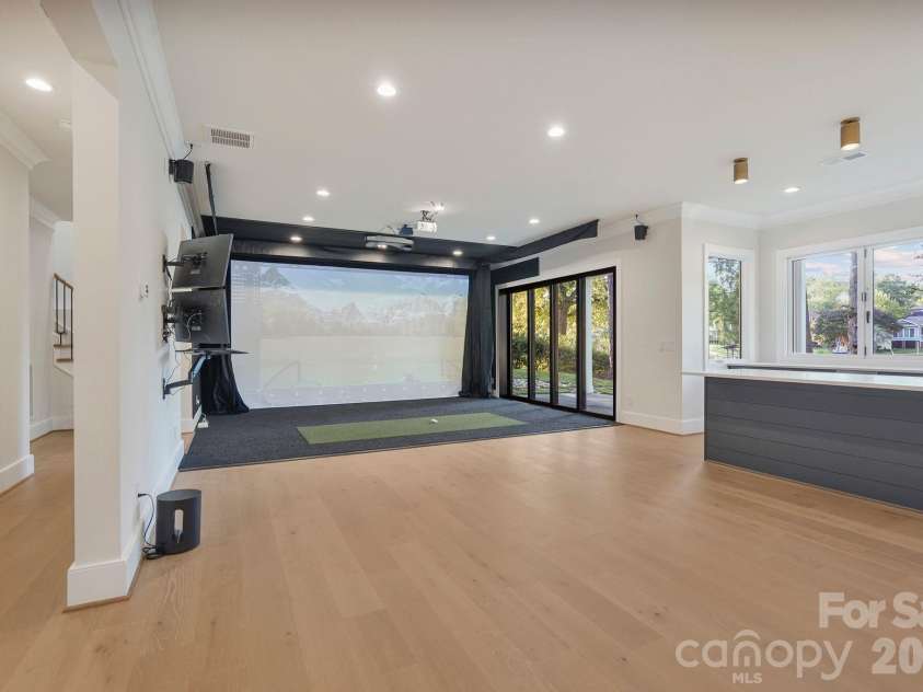 21216 Rio Oro Drive, Cornelius, NC 28031.  MLS# CAR4425303, YatesRealty ID 45943. Open view of the golf simulator and entertainment space, featuring a quad-stack sliding glass door that opens to the covered porch for seamless indoor-outdoor living.