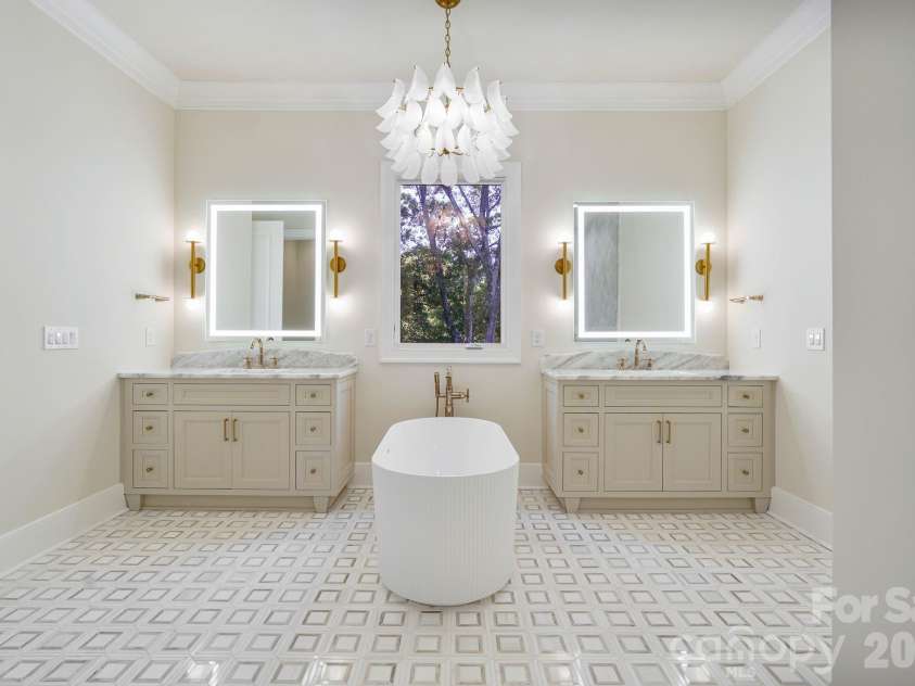 21216 Rio Oro Drive, Cornelius, NC 28031.  MLS# CAR4425303, YatesRealty ID 45943. Spa-inspired primary bath featuring separate his-and-hers vanities, a sculptural freestanding tub with statement lighting, luxury illuminated mirrors, and a large window that fills the space with natural light.