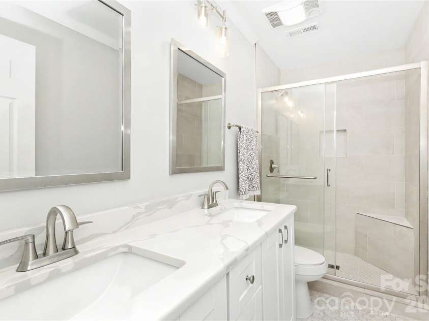 2701 Creekbed Lane, Charlotte, NC 28210.  MLS# CAR4411182, YatesRealty ID 47954. Beautifully updated Primary Bath with dual under-mount sinks, quartz counter, elegant porecelain tile flooring and shower surround complete with seamless glass door.