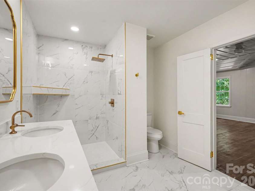 601 Marion Sims Drive, Lancaster, SC 29720.  MLS# CAR4404710, YatesRealty ID 48048. Elegantly updated primary bath highlighting a marble-tiled walk-in shower with gold rain showerhead trim, double-sink vanity, and direct suite access.