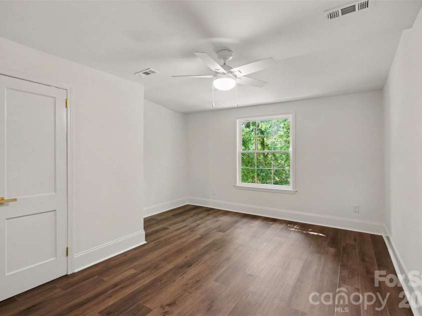 601 Marion Sims Drive, Lancaster, SC 29720.  MLS# CAR4404710, YatesRealty ID 48048. Quiet, light-filled bedroom situated off the kitchen, featuring a large window overlooking lush greenery in the back yard, stylish wide-plank flooring, and a sleek ceiling fan.
